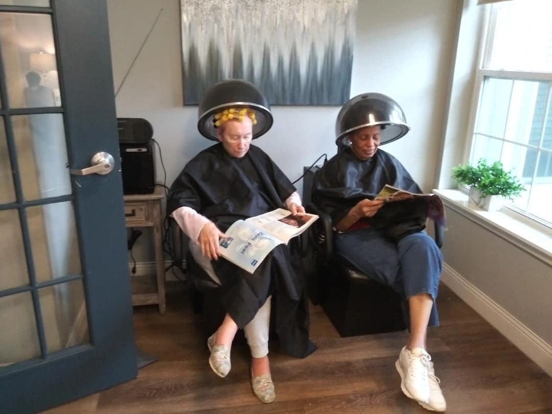 Two women sitting on a bench with their hair drying caps.
